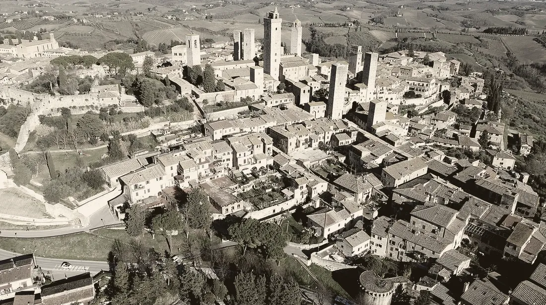 San Gimignano aus der Luft: Auf einem Höhenrücken ragt ein Bündel hoher viereckiger Türme aus den Ziegeldächern auf.